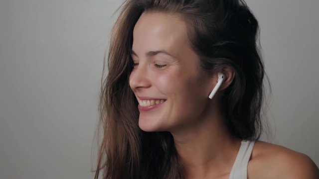 Portrait of a beautiful young, in a leather jacket with airpods in her ear, listens to music. Student dancing happy earpods handsfree bluetooch girl smiling, looking down.
