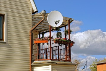 round satellite dish on an open balcony with flowerpots and flowers on a private house