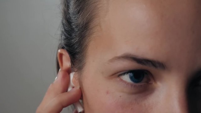 Portrait of a beautiful young, in a leather jacket with airpods in her ear, listens to music close up macro super. Student dancing happy earpods handsfree bluetooch girl smiling, looking down.