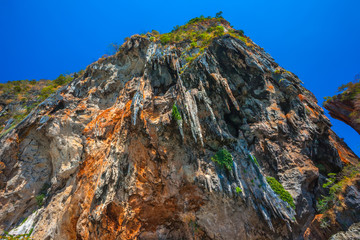 Obraz premium Look up at the sheer hanging orange brown limestone cliff like stone icicles hanging above people bathing in the sea. Phra Nang Princess Cave Beach, Krabi, Thailand.