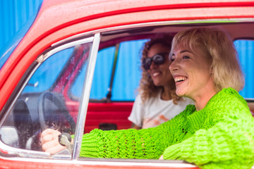 Couple of women friends traveling in a rainy holiday day. Colors and young middle age woman together in friendship inside a red vintage beautiful car. Independent ladies on travel