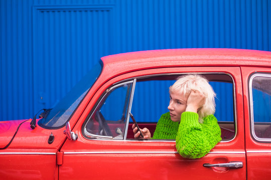 Travel and fashion concept with attractive people lady caucasian inside a red retro beautiful car using mobile phone technologyh internet connected to check map and discover new places. Colors image.