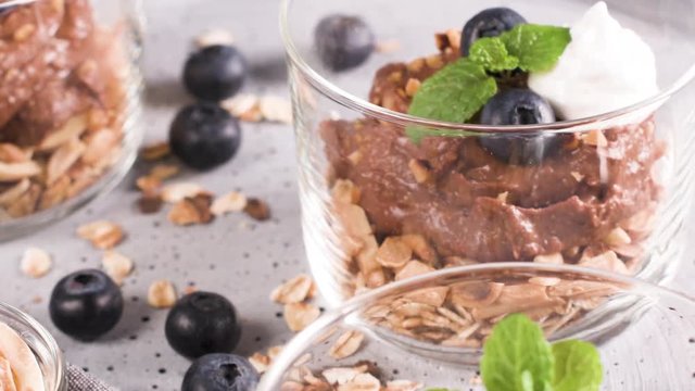 Glass cups of chocolate and chestnuts mousse with roasted almonds and oats decorated with black berries and mint leaves.