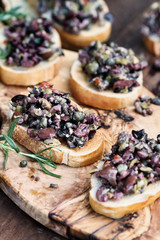Homemade mixed Olive Tapenade made with garlic, capers, olive oil, Kalamata, black and green olives spread over toasted bread. Selective focus on center canape with blurred background.