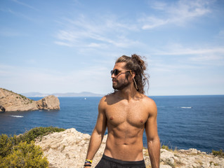 young man with long hair wearing sunglasses posing next to the coast