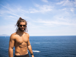 young man with long hair wearing sunglasses posing next to the coast