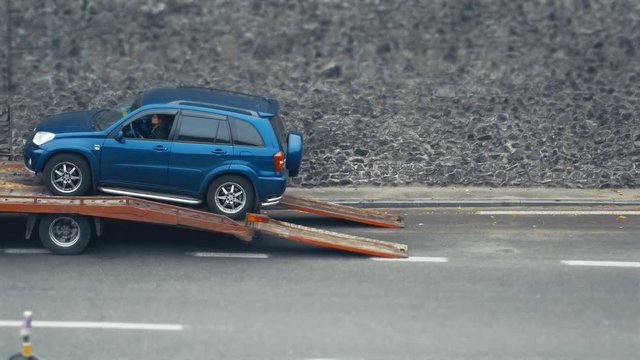 Tow truck takes broken suv. Young woman inside the car. Rescue roadside mechanic helps to pick up the vehicle. Time lapse