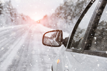 White car on a winter road through a snow covered forest.