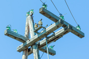 Old wooden pole and post with electrical power line against background of blue sky