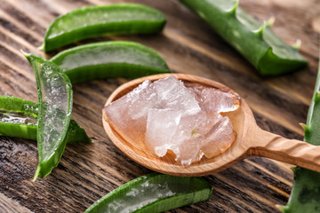 Spoon with peeled aloe vera and green leaves on wooden table