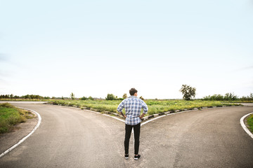 Young man standing at crossroads. Concept of choice - obrazy, fototapety, plakaty