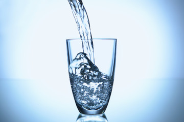 Pouring of water in glass on light background