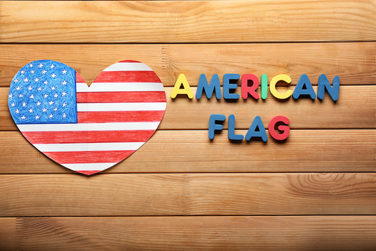 Heart shaped drawing of American national flag with color letters on wooden table