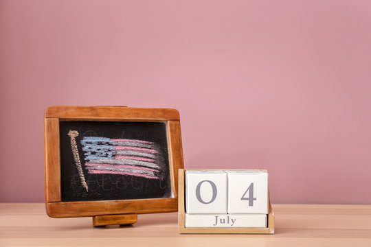 Chalkboard with drawing of American national flag and calendar on wooden table. 4th July celebration