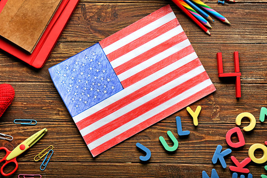 Drawing of American national flag with color letters and stationery on wooden table. 4th July celebration