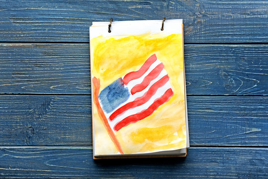 Sheet with watercolor painting of American national flag on color wooden table