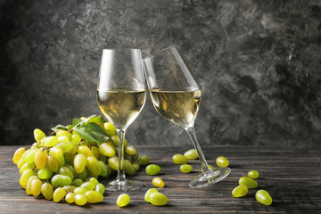Glasses of white wine with ripe grapes on wooden table