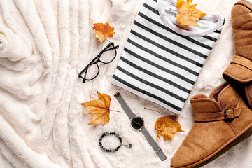 Stylish outfit with accessories and autumn leaves on fluffy fabric