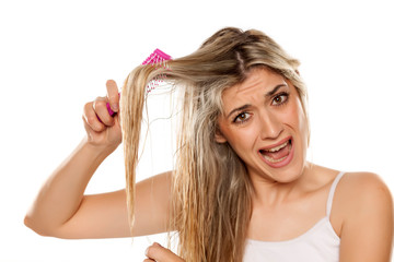 desperate blond woman combing her messy wet hair on white background