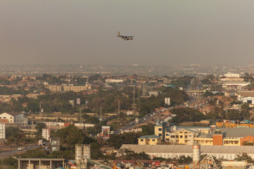 High view point cityscape of Accra, Ghana. Airplane flying low over traffic on Spintex Road going East with billboards, constructions sites, wasteland and business buildings and hazy horizon 