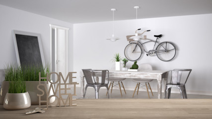 Wooden table, desk or shelf with potted grass plant, house keys and 3D letters making the words home sweet home, over living room with sofa and table, interior design, blur background