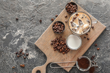 Glass cup of cold coffee with beans and milk on wooden board
