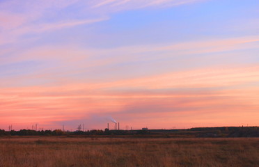 Orange sunset in summer over black earth against blue sky