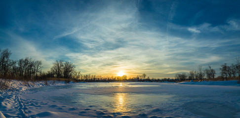 A winter sunset over a small, ice and snow covered lake. Can be used as a sky replacement. Panorama.