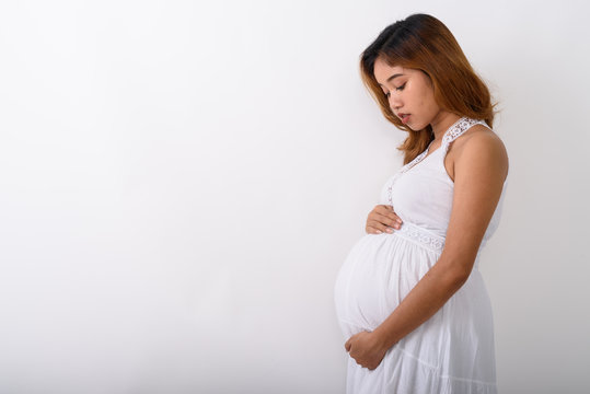 Profile view of young Asian pregnant woman looking at her stomac