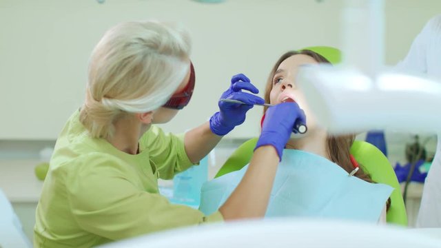 Dentist working with dental polymerization lamp in oral cavity. Young woman during dental procedure. Female dentist in safety goggles. Patient with open mouth in dentist chair