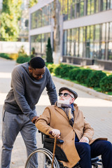 senior disabled man in wheelchair and african american man talking on street
