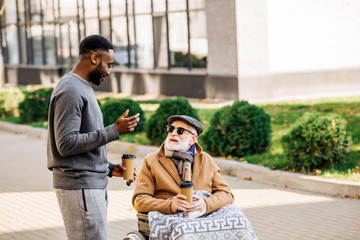 smiling senior disabled man in wheelchair with plaid and african american man spending tome...