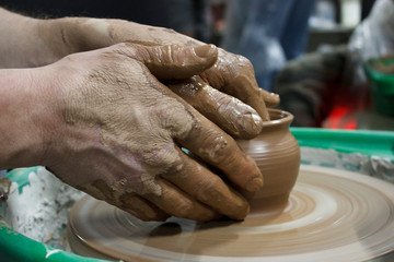 male hands of a student in pottery training courses, reportage photography. making a pot of red clay on a potter's wheel.