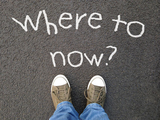 feet standing on road with where to now question written on asphalt - indecision confusion choice...