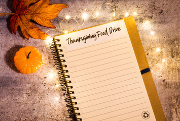 Thanksgiving Food Drive list concept on notebook surrounded with bright leaves and decorative lights, flat lay