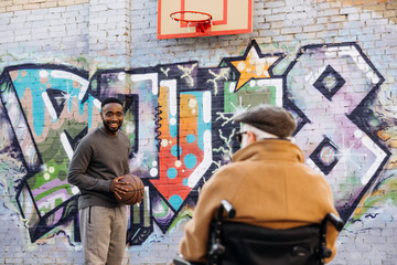 rear view of senior disabled man in wheelchair looking at african american man playing basketball...