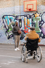 back view of senior disabled man in wheelchair looking at african american man playing basketball...