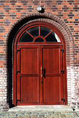 Red large semicircular wooden closed door with glazed in a brown brick wall