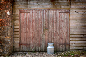 Traditional milk churn by a barn door