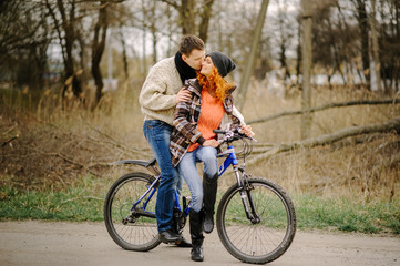 Fototapeta na wymiar Couple in love is riding the bicycle in the park. Active people. Outdoors. Autumn couple wearing in autumn clothes. Funny couple are getting ready for autumn sale