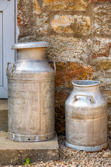 Two traditional milk churns on a door step
