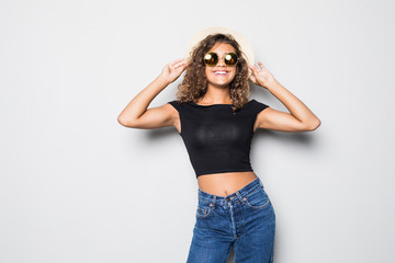 Smiling curly hair woman in , straw hat and sunglasses posing while looking at the camera over white background