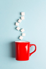 Red mug with sugar cubes on a blue background. Sugar addict. Diabetes concept. .