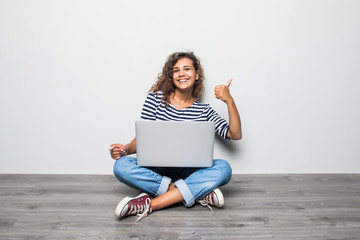 Portrait of satisfied woman with thumbs up laptop on legs and sitting in lotus pose on the floor...
