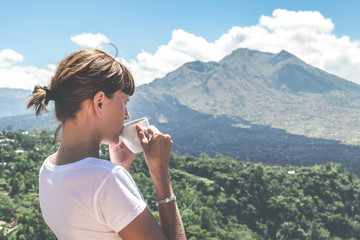 Young woman drinking coffee on a mountain background. Volcano Batur, Bali island. Indonesia.