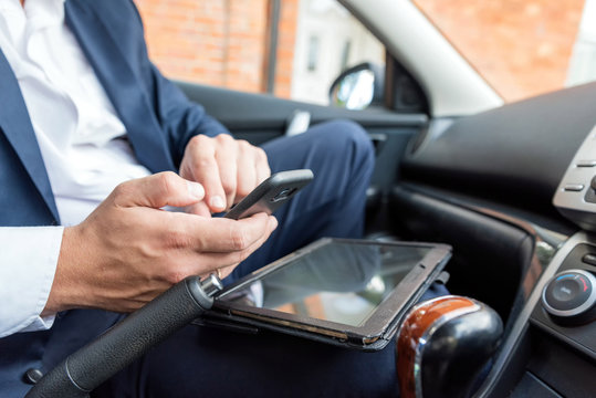 Businessman working on tablet and smartphone inside car on bright day