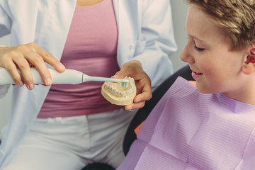 Female dentist explaining boy how to clean his teeth on a tooth model