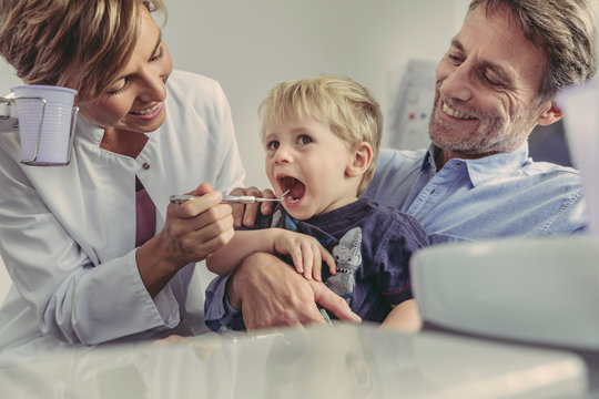 Female dentist examining little boy, sitting on his father's lap