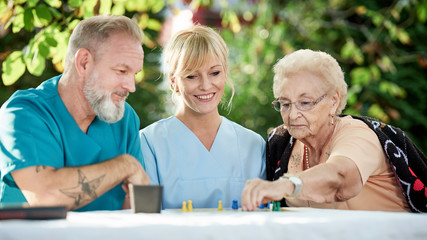 Pfleger spielen mit Seniorin ein Brettspiel