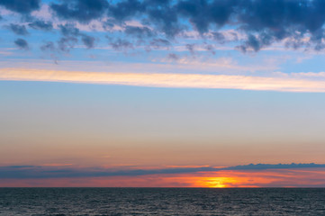 Sunset over the sea. Reflection of sunlight in the sea waves. Red and yellow sky in the rays of the sunset.